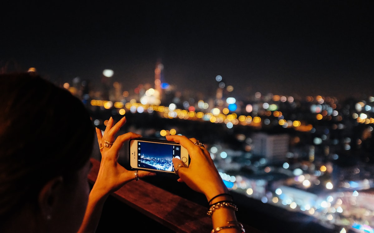 Mãos segurando celular com as luzes da cidade à noite ao fundo — atendimento fora do horário comercial