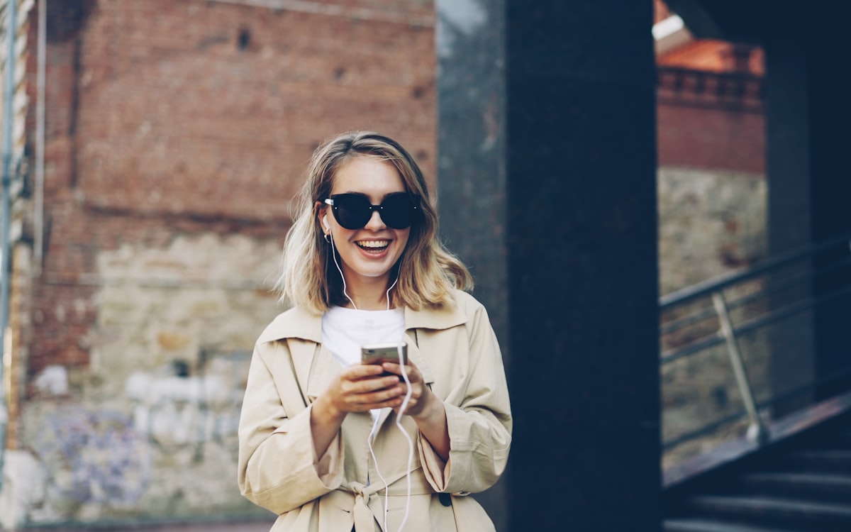 Mulher sorrindo ao usar o celular na rua — acesso à internet pelo celular e atendimento mobile-first
