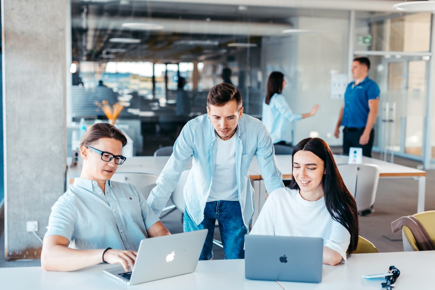 Três pessoas trabalhando em laptops Apple numa mesa de escritório moderno — equipe colaborando no que parece ser análise de dados de clientes em CRM