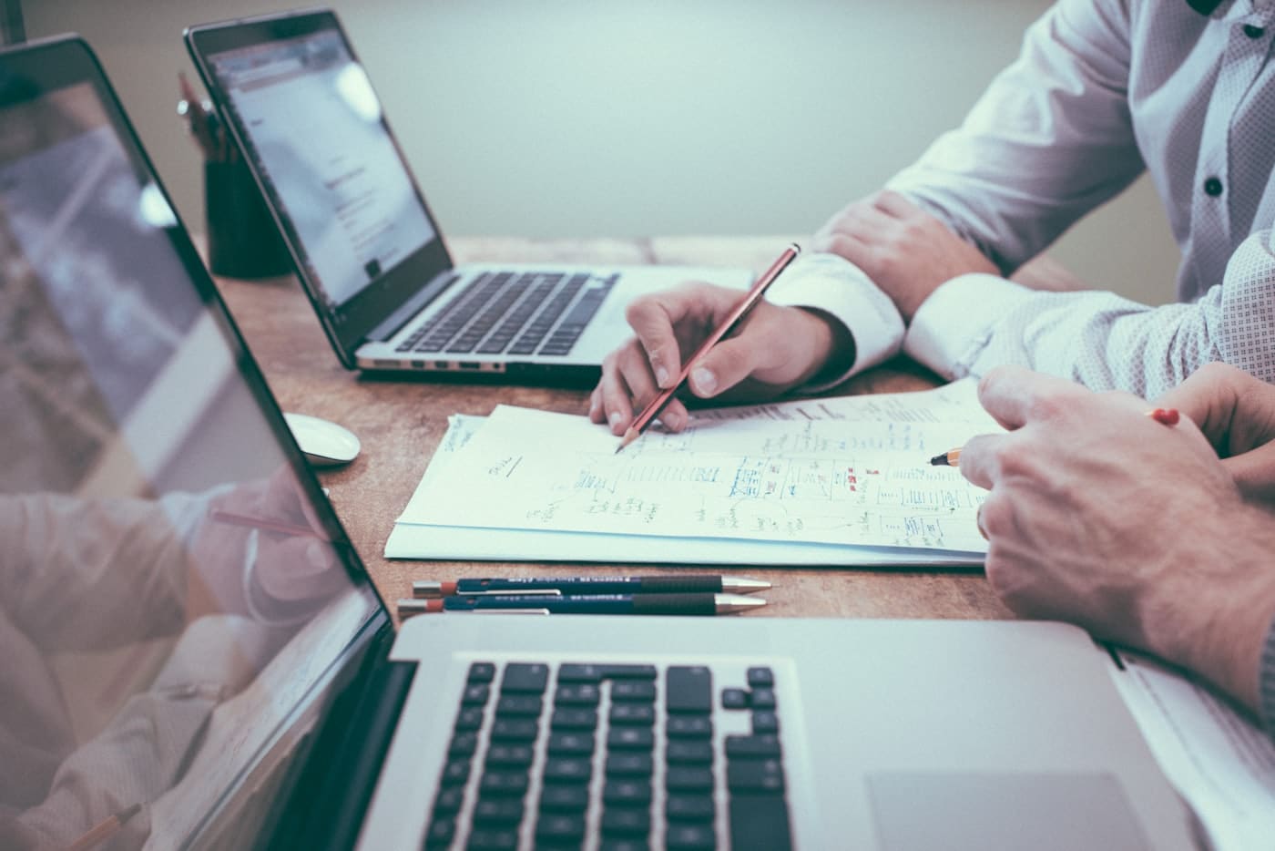Duas pessoas trabalhando em mesa com notebooks e papel com planilhas e gráficos, simulando análise de comparativo de CRM gratuito